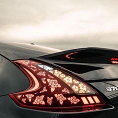 the back end of a black car with red flowers on it's tail lights