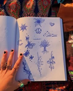 a woman's hand is holding an open book with drawings on it and the pages are lined in blue ink