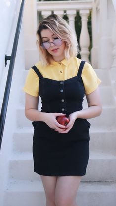 a woman with glasses is standing on the stairs and holding an apple in her hand