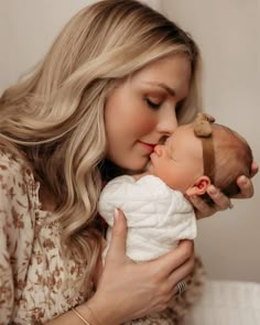 a woman holding a baby in her arms and kissing it's face with the other hand