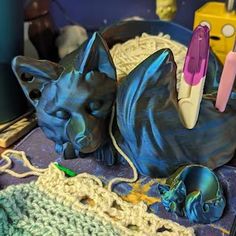 a cat statue laying on top of a table next to some crocheted items