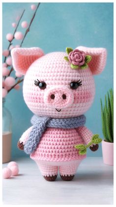 a crocheted pig with a scarf and flower on it's head standing next to a potted plant