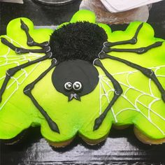 a green cake with black icing and a spider on it's face, sitting on top of a table