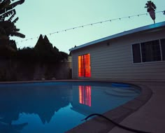 a house with a pool in the backyard at night, lit up by red lights