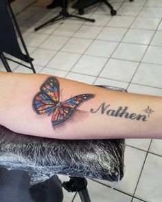 a colorful butterfly with the name nalben tattooed on it's arm, sitting on a chair