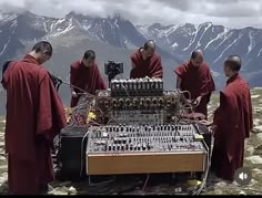 four monks in red robes are looking at an electronic device on top of a mountain