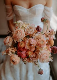 a woman in a wedding dress holding a bouquet of pink and orange flowers on her arm