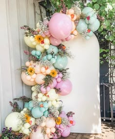 a bunch of balloons hanging from the side of a wall next to flowers and plants