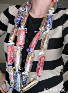 a woman is holding several candy bars wrapped in plastic wrap around her neck and wearing a black and white striped shirt