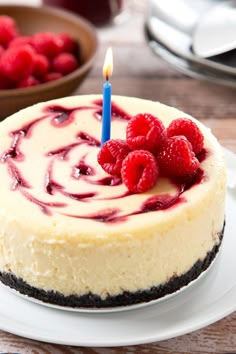 a cheesecake with raspberries on top and a lit candle in the middle