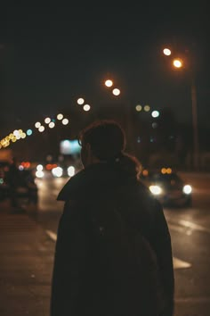 a man standing on the side of a road at night with cars passing by in the background