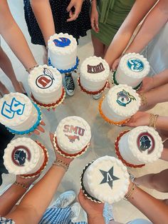 a group of people standing around a table with cakes on it's sides and hands in the middle