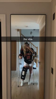 a woman with crutches and knee braces standing in front of a mirror