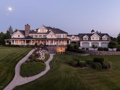 a large house with lots of windows and lights on it's front porch, surrounded by lush green grass