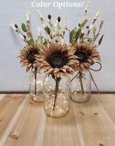 three mason jars with sunflowers and greenery in them on a wooden table