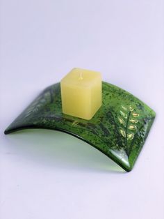 a candle sitting on top of a green leaf shaped plate with a square candle in the middle