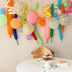 a table topped with a cake covered in frosting next to balloons and confetti