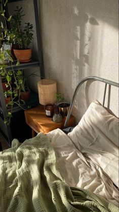 an unmade bed sitting next to a shelf filled with potted plants