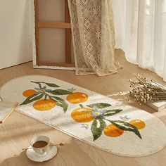 a white rug with oranges on it next to a cup of coffee and an open window