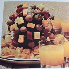 an arrangement of fruit and appetizers on a platter with glasses of juice