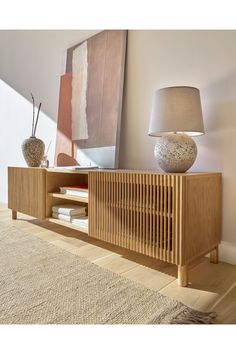 a wooden cabinet with a lamp on top of it next to a painting and rug