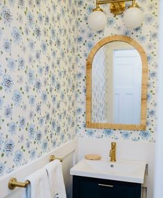 a bathroom with blue and white wallpaper, gold faucet, sink and mirror