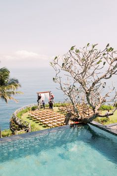 an outdoor wedding setup with chairs and a tree next to the swimming pool, overlooking the ocean