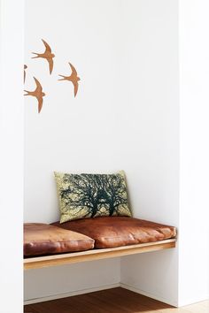 three birds flying in the air above a wooden bench with pillows on top of it