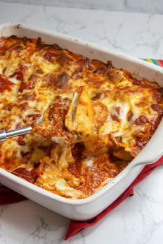 a casserole dish with meat and cheese being scooped from the casserole