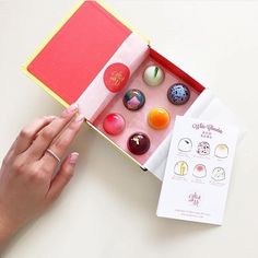 a woman's hand is holding an open box with different types of candies