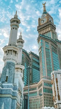 two tall buildings with clocks on them against a blue sky and white clouds in the background