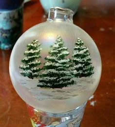 a glass ornament with trees on it sitting on top of a wooden table