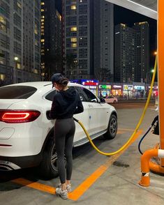 a woman pumping gas into her car at a gas station in the middle of a city