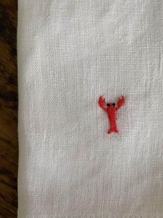 a small red teddy bear embroidered on a white linen napkin with a wooden table in the background