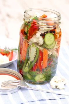 a mason jar filled with pickles, cucumbers, tomatoes and other veggies