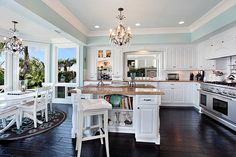 a large kitchen with white cabinets and an island in the middle is decorated with chandeliers