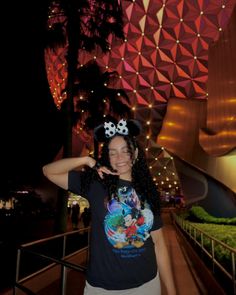 a woman standing in front of a building with lights on it's side and mickey mouse ears on her head