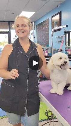 a woman standing next to a white dog on top of a purple table in a room