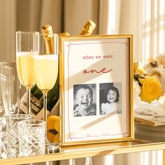 two champagne flutes are sitting on a table next to a wine glass and photo frame that says, when we were one