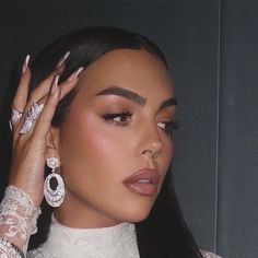 a close up of a person wearing jewelry and holding her hand near her face with both hands