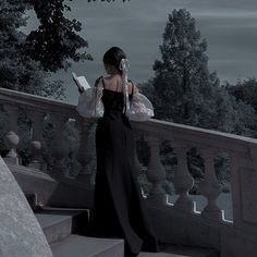 a woman is standing on some stairs and looking at her cell phone while wearing a long black dress