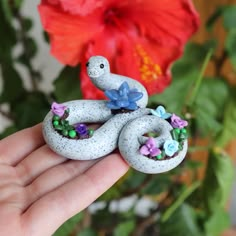 a hand holding a small white snake figurine in front of a red flower