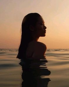 a woman in the water at sunset with her head above the water's surface