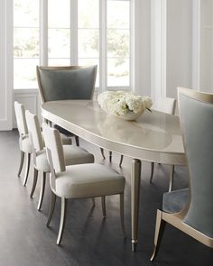 a dining room table with chairs and a vase on top of it in front of two windows