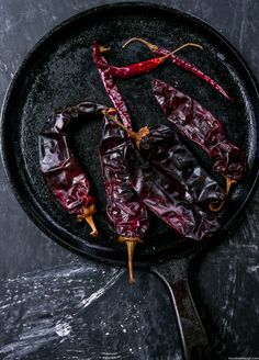 three chili peppers in a cast iron skillet on a black surface with a spoon