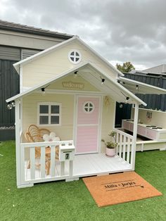 a small white house sitting on top of a lush green field next to a pink door