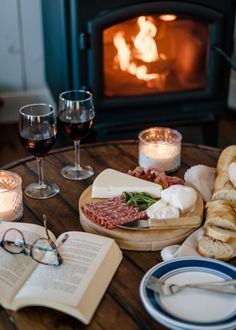 a table with bread, meats and glasses of wine next to an open book