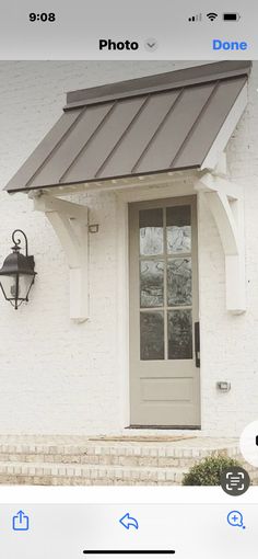 an image of a white house with a gray door and brown awning on it