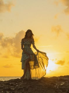 a woman in a dress standing on rocks at sunset