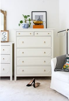 a white dresser sitting in a bedroom next to a chair and table with shoes on it